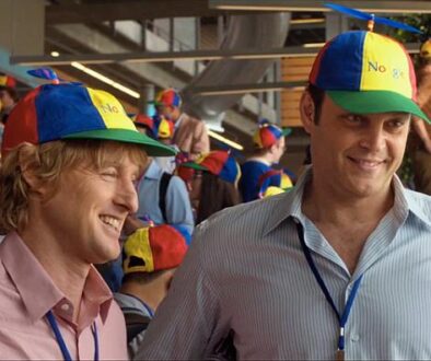 Dos hombres sonrientes con gorras coloridas en un ambiente corporativo concurrido.